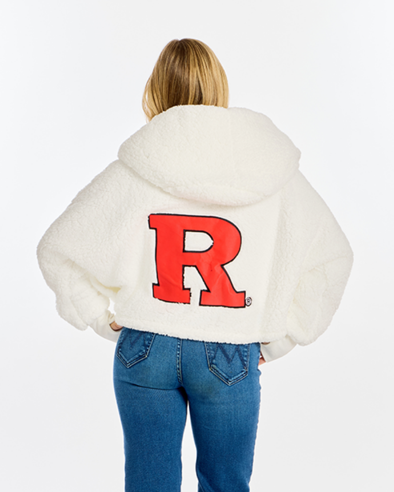 A woman viewed from behind wearing a white sherpa hoodie with a large red block letter 'R' on the back, paired with blue jeans, against a plain white background.
