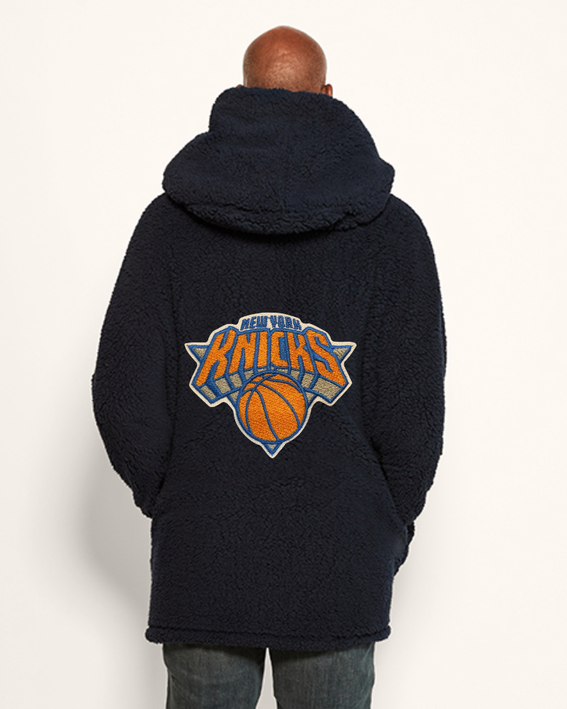 Person wearing a navy hoodie with New York Knicks logo on the back against a white background