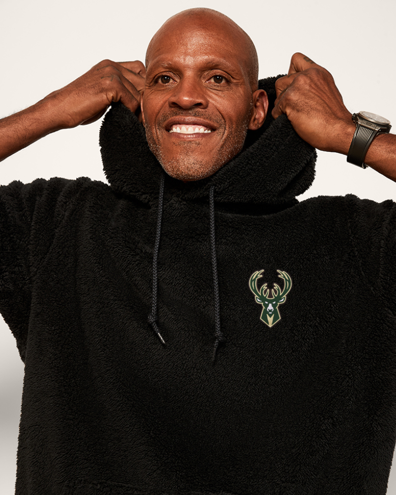 Man wearing a black hoodie with a bucks logo, smiling against a white background