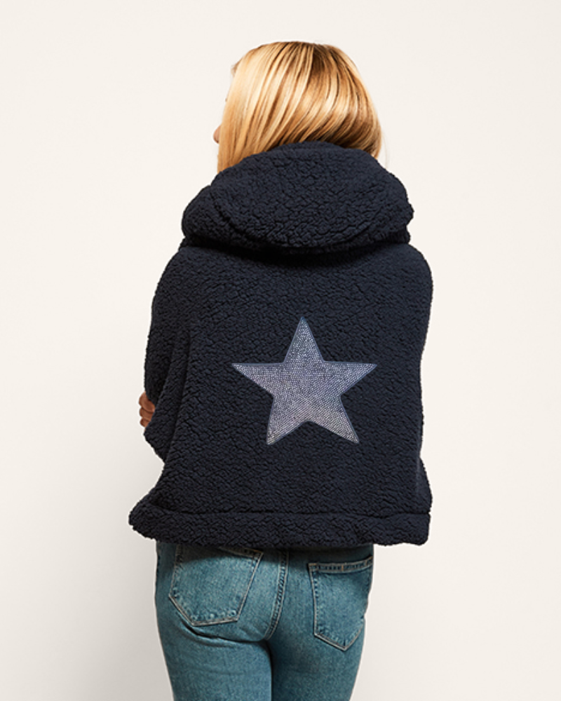 Person wearing a navy blue jacket with a bedazzled star design on the back against a white background