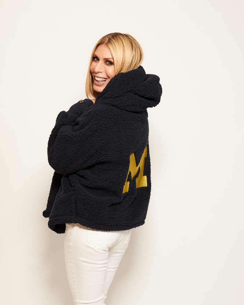 Person wearing a navy hoodie sherpa lounger with a gold university of michigan letter 'M' on a white background