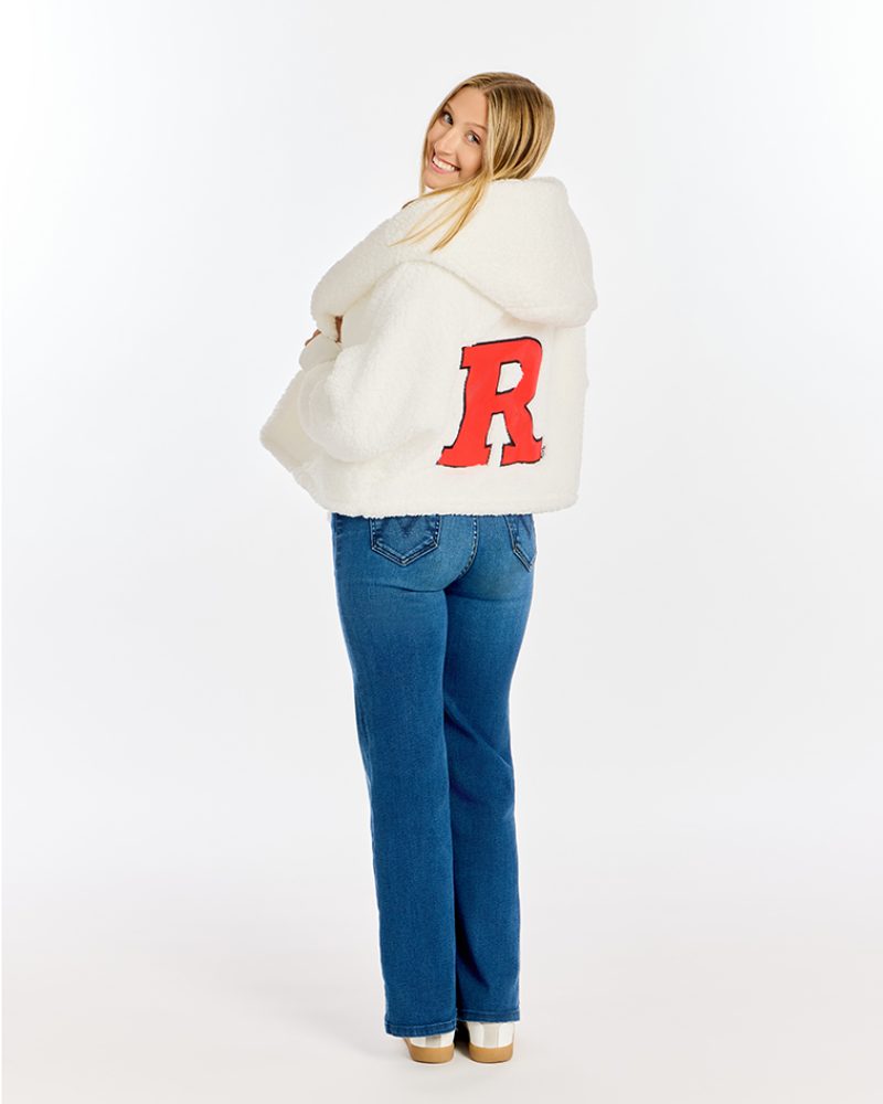 A woman wearing a white sherpa fleece hooded jacket with a large red letter 'R' on the back, paired with blue jeans, photographed against a seamless white studio background.