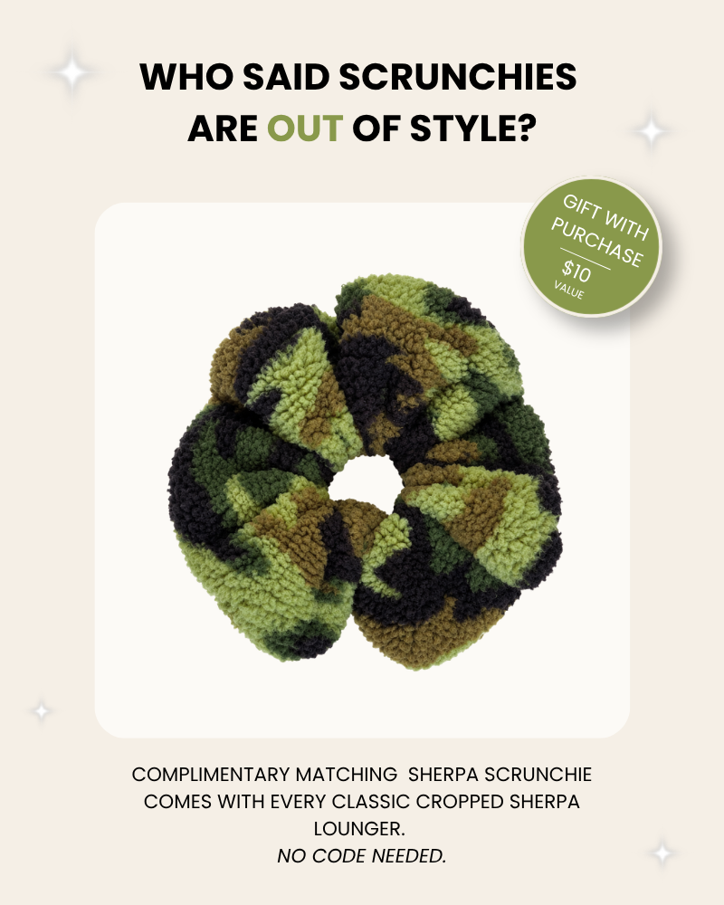A green and black camouflage sherpa scrunchie is centered on a cream background with promotional text above and below. A green circular badge says 'Gift with Purchase $10 Value.