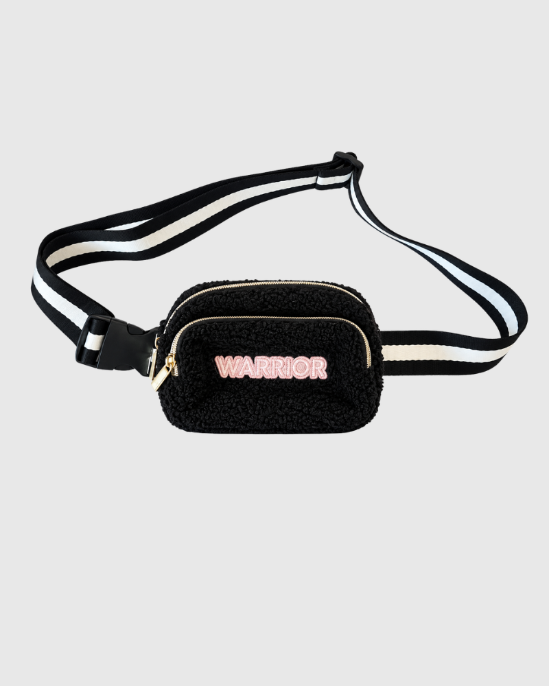 A black sherpa fanny pack with a black and white striped adjustable strap, featuring a gold zipper and the word 'WARRIOR' in pink letters on the front.