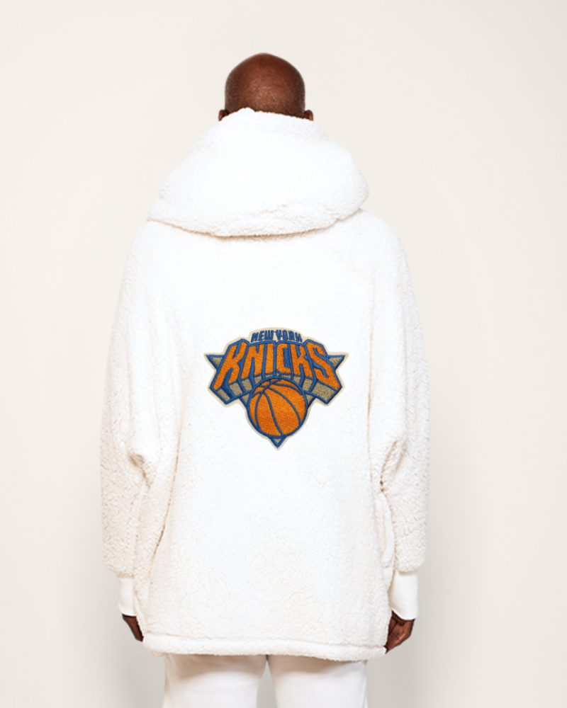 Person wearing a white hoodie with a Knicks logo on the back against a plain background