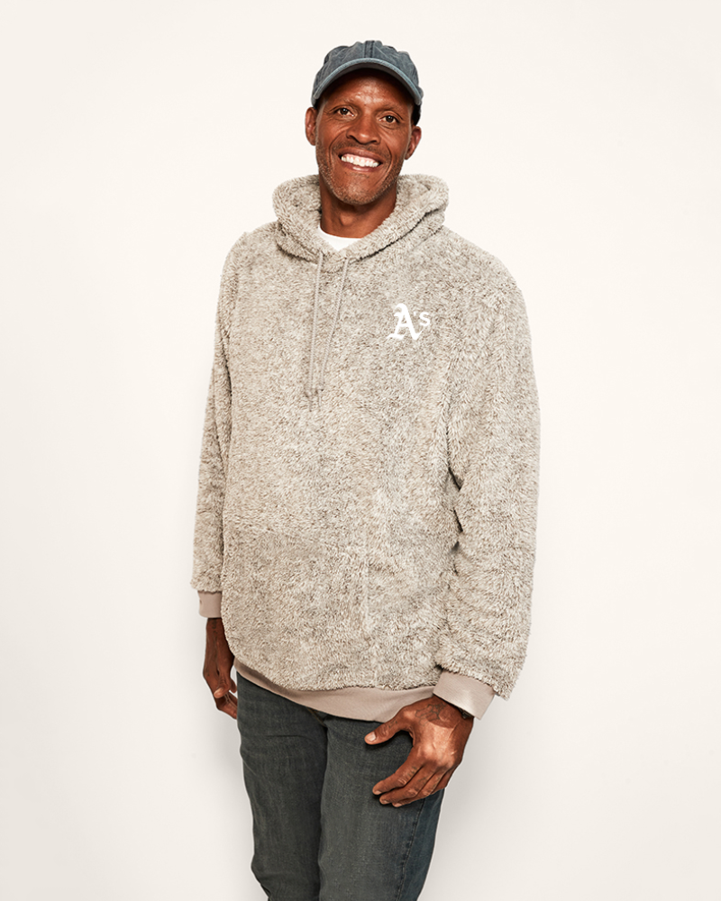 Man wearing a grey hoodie with the athletics logo and a cap on a white background