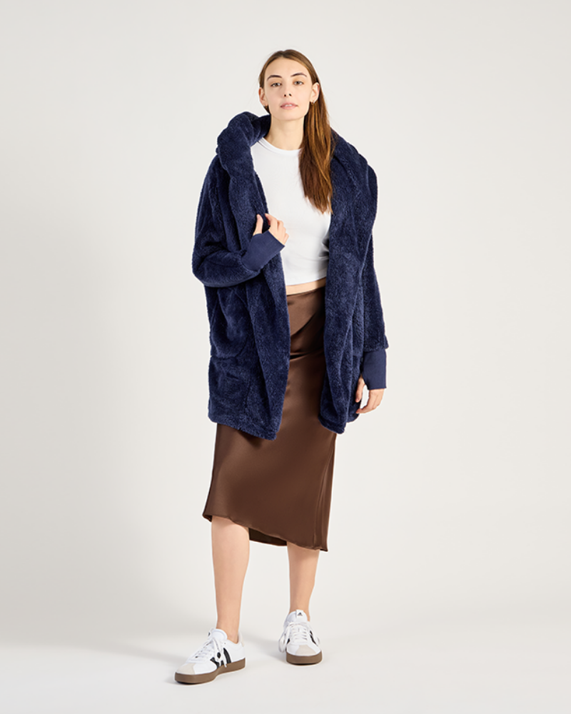 Person wearing a navy blue oversized coat, white shirt, brown skirt, and white sneakers on a white background