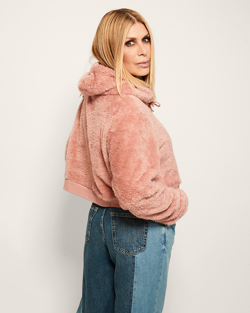 Woman wearing a pink fluffy jacket and blue jeans against a white background