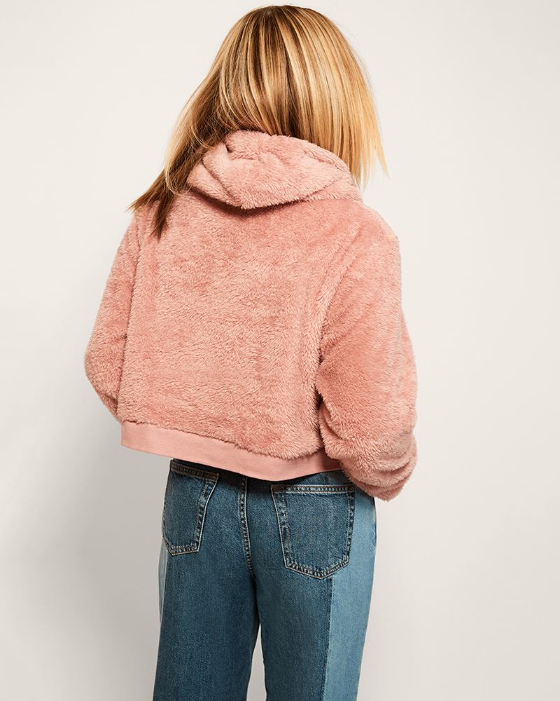 Person wearing a pink fleece jacket and blue jeans on a plain background