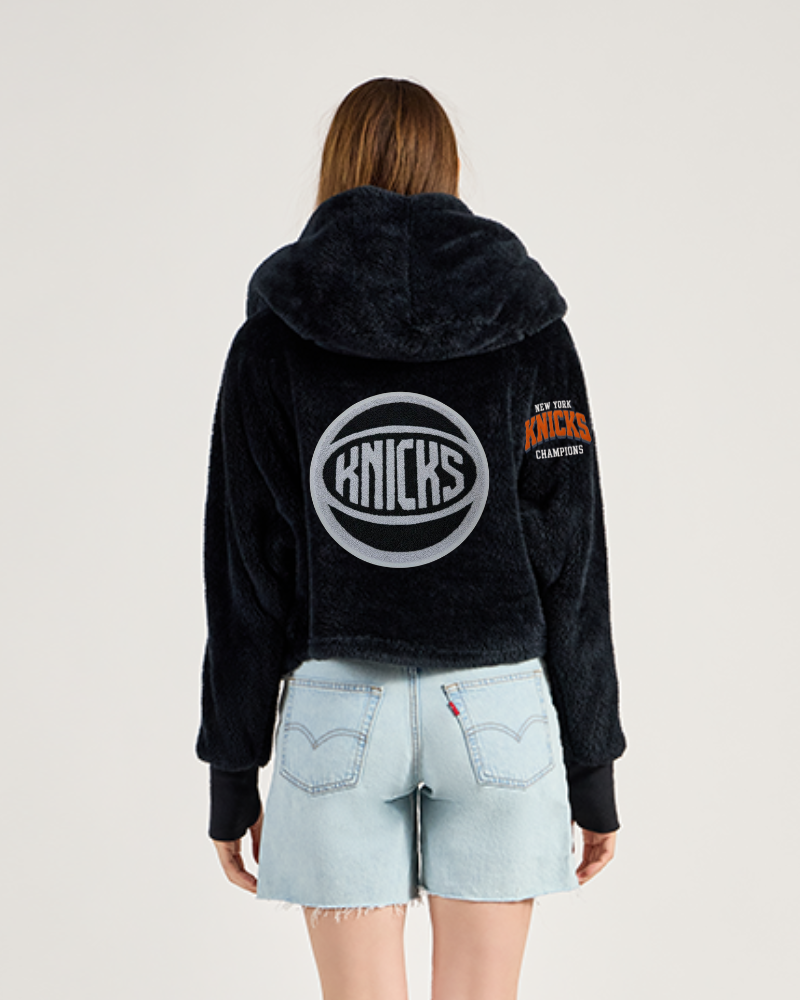 Person wearing a black lounger with 'Knicks' logo on the back, standing against a light gray background
