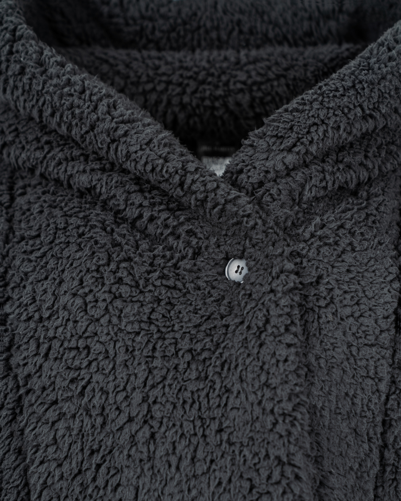 Close-up of a textured black sherpa jacket garment with a button.