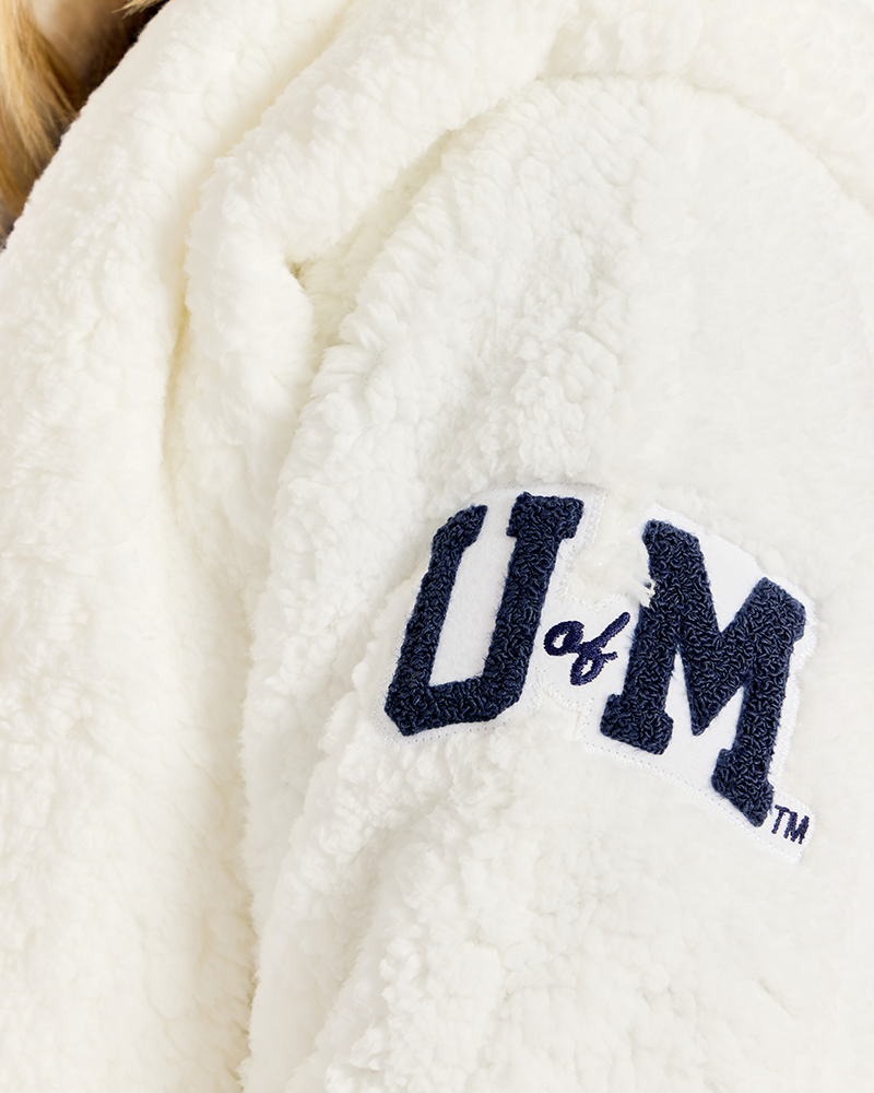 Close-up of a white sherpa fleece garment with a navy blue embroidered 'U of M' logo on the bicep.