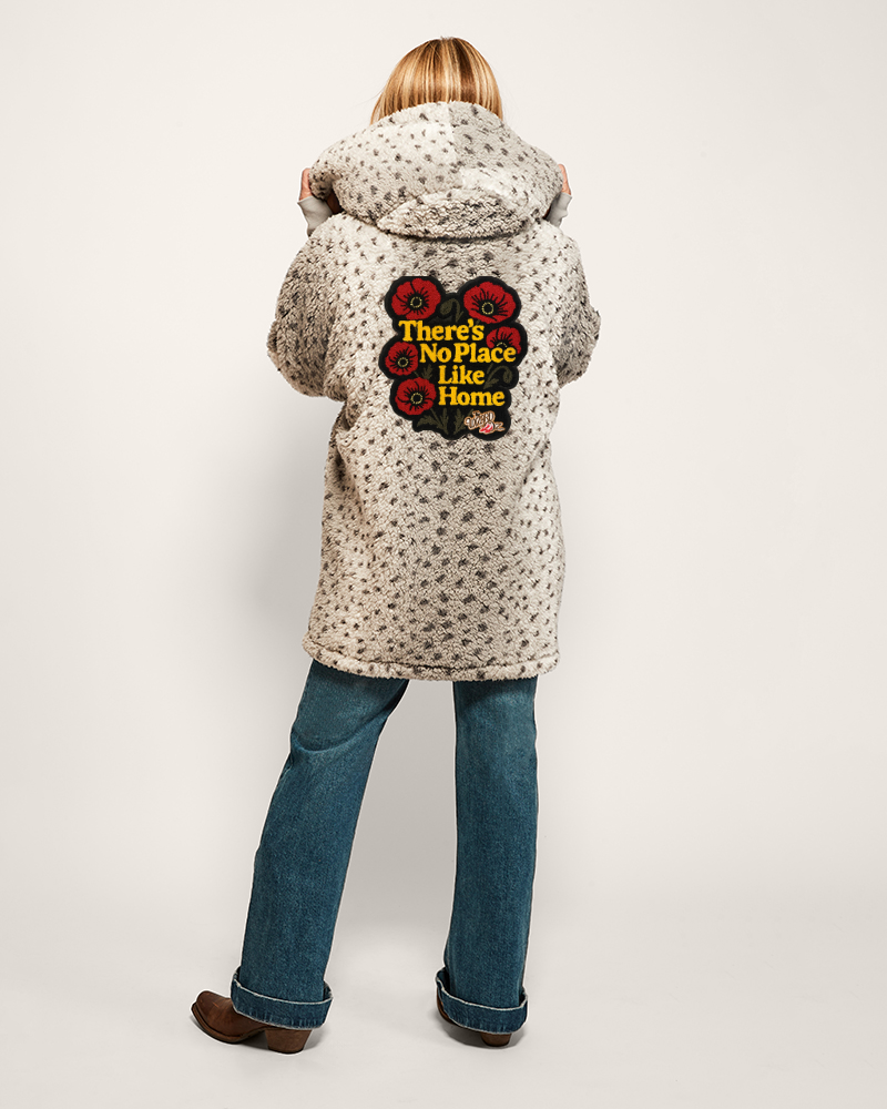 Person wearing a patterned coat with a 'There's No Place Like Home' quote on the back, standing against a white background.