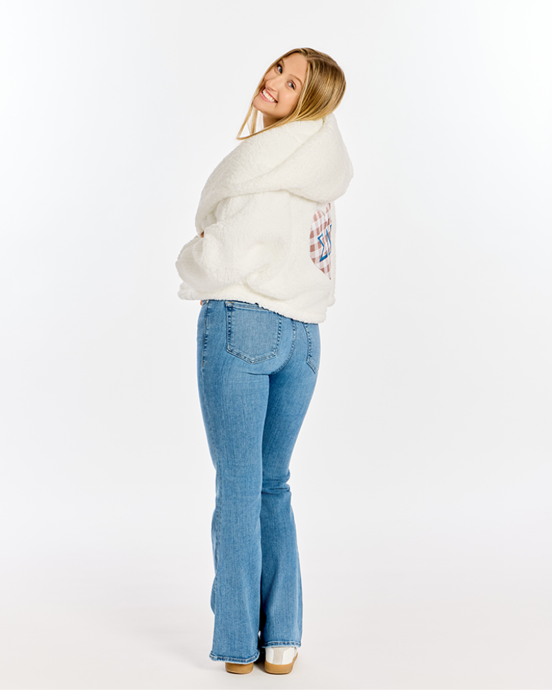 A woman posing from the back wearing a fluffy white hooded sweatshirt with a colorful graphic on the back, paired with light blue flared jeans and white sneakers, against a plain white studio background.
