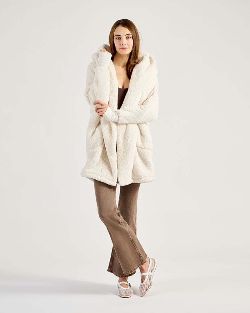 Woman wearing a cream-colored cardigan over a black top and brown pants on a white background