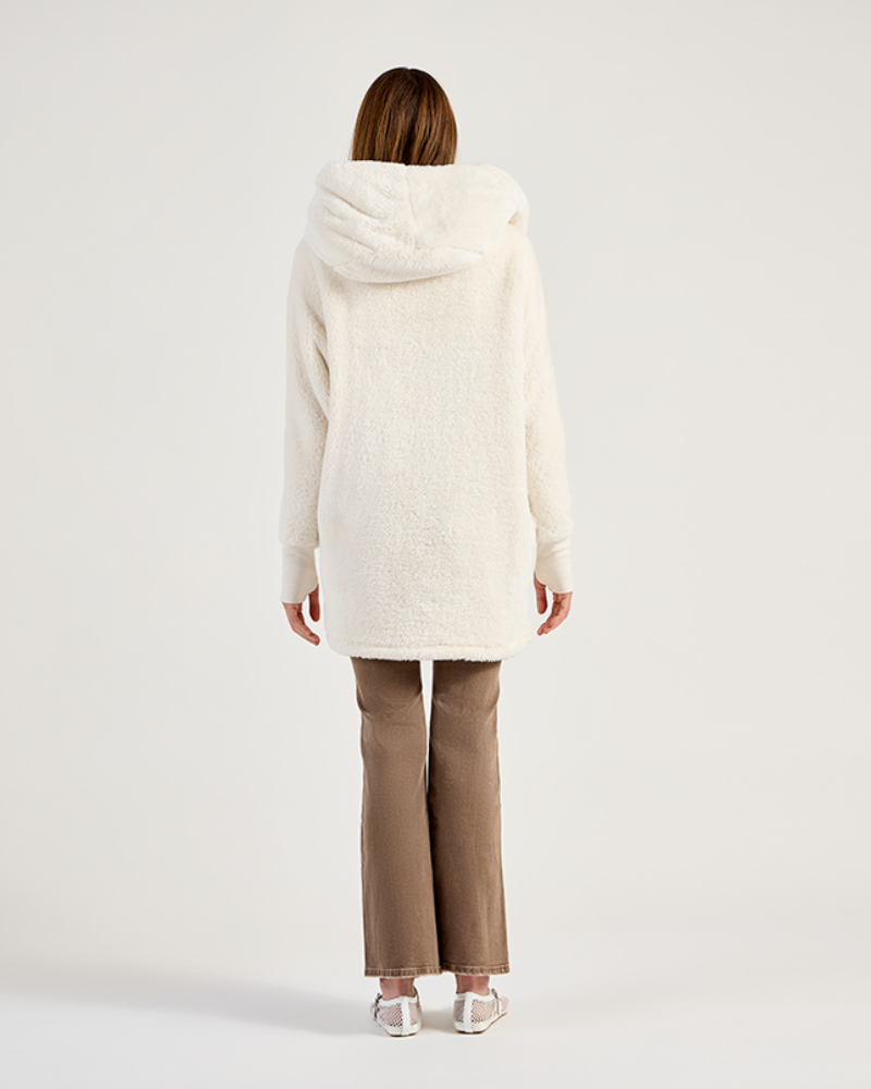 Person wearing a white hooded coat and beige pants on a light gray background