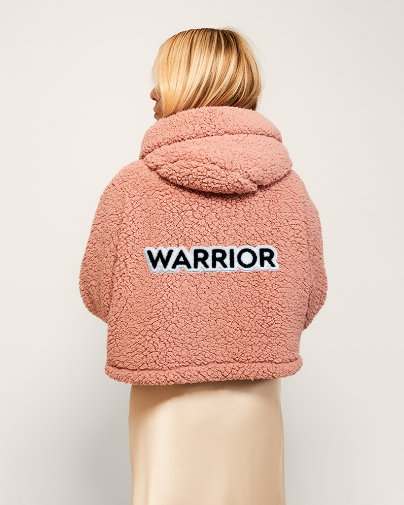 Pink sherpa jacket with 'WARRIOR' text on the back against a light background
