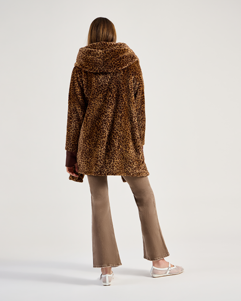 Person wearing a leopard print coat and beige pants on a white background