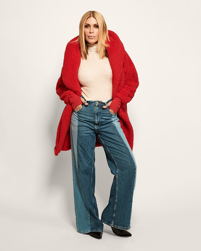 Person wearing a red cardigan, white top, and blue jeans on a plain background