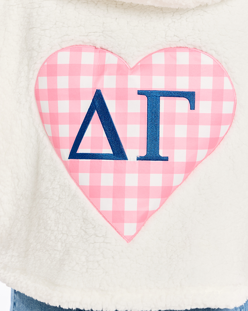 Close-up of a cream sherpa fleece garment featuring a large pink and white gingham heart applique with navy blue Greek letters Delta and Gamma.