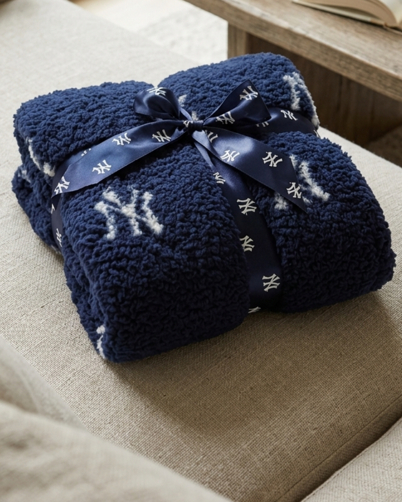 Navy blue blanket with white logo tied with a ribbon on a beige couch.