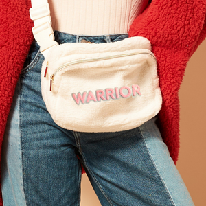 Beige fanny pack with 'Warrior' text worn by a person in a red jacket and blue jeans.