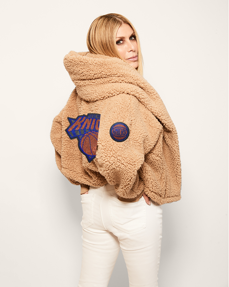 Person wearing a beige fleece jacket with patches on a plain background