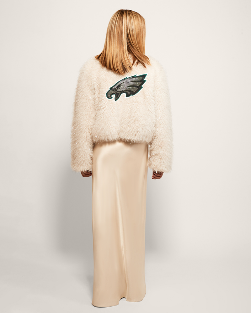 person wearing white faux fur jacket with Philadelphia eagles logo