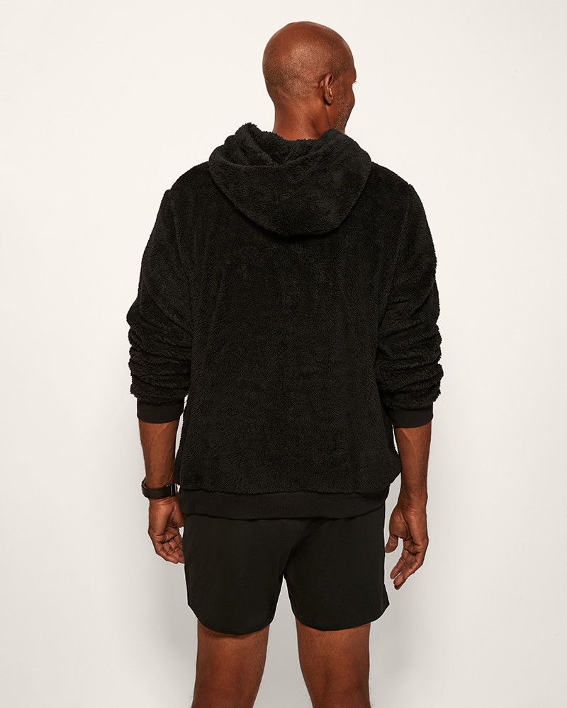Person wearing a black hoodie and shorts on a white background