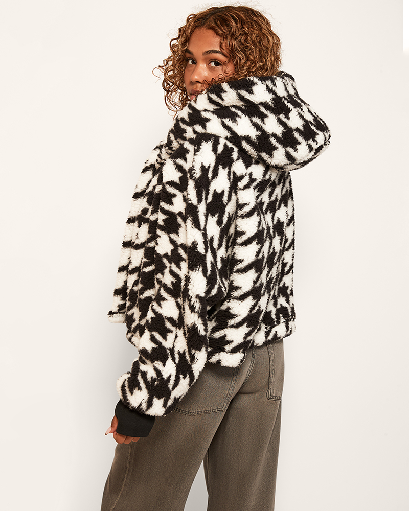 Person wearing a black and white patterned jacket on a plain background