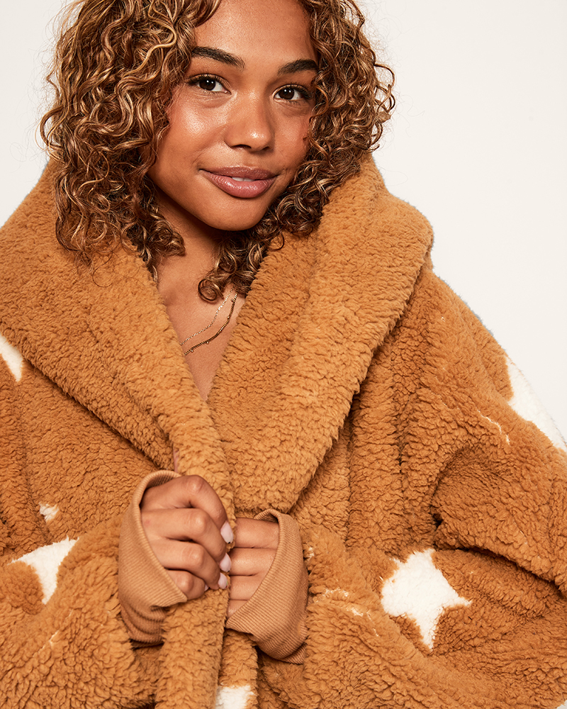 Woman wearing a brown fleece robe with white star patterns on a plain background