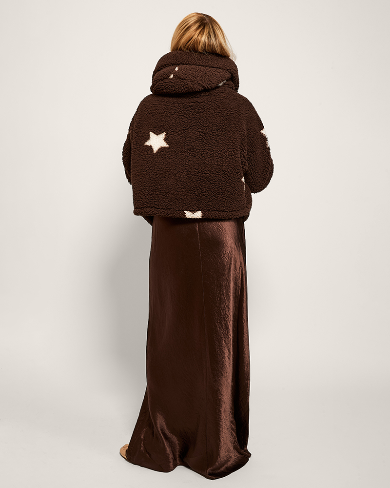 Person wearing a brown fleece jacket with star patterns and a long brown skirt on a white background