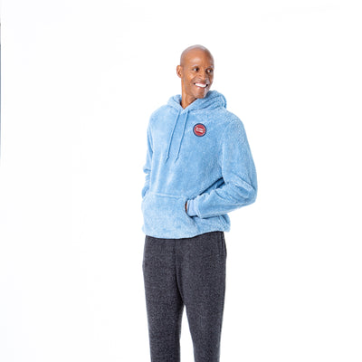Side view of man with hands in the hoodie pocket wearing light blue sherpa hoodie with a front kangaroo pocket and drawstring hood, featuring small circular Detroit Pistons embroidery on the left chest.