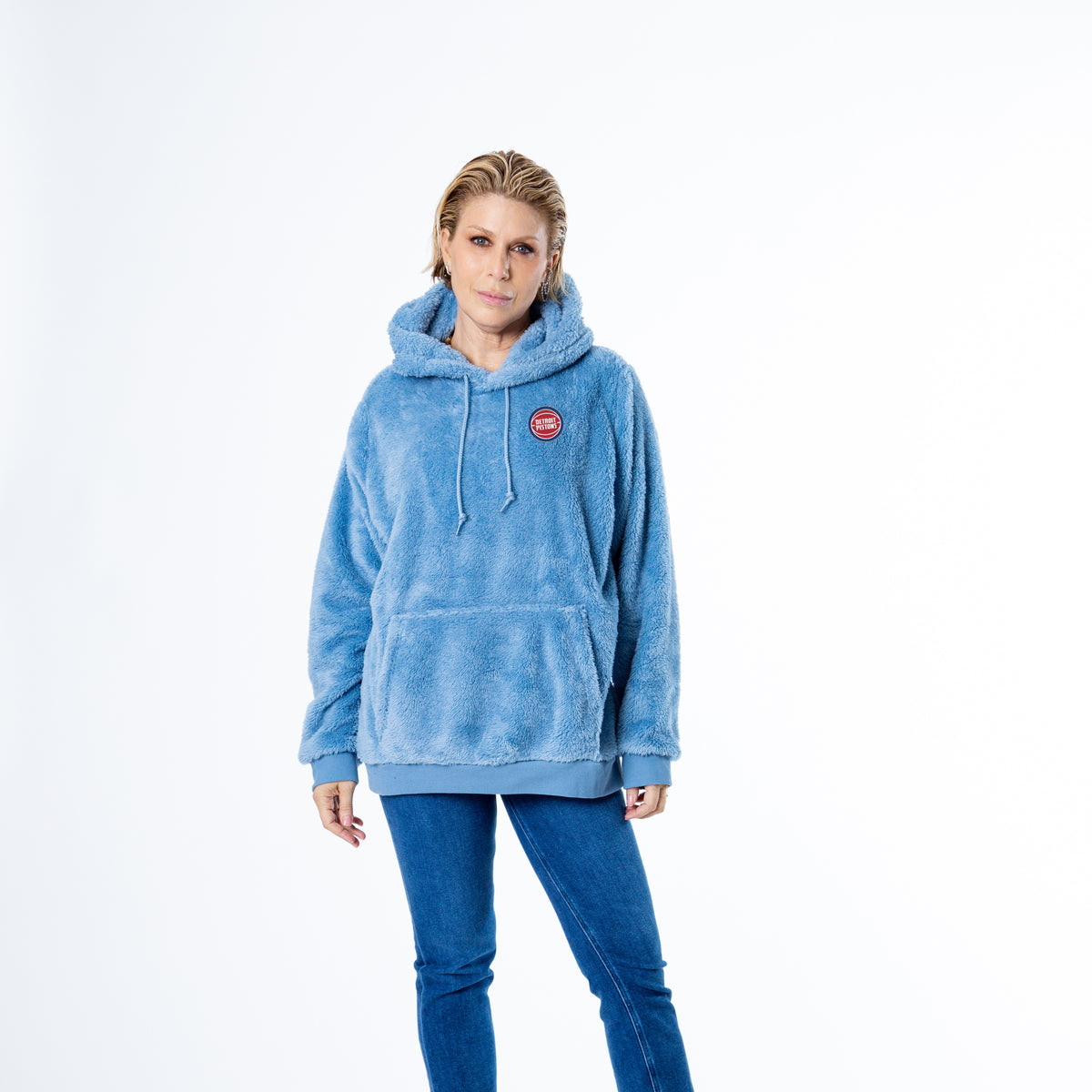 Woman facing forward wearing light blue sherpa hoodie with a front kangaroo pocket and drawstring hood, featuring small circular Detroit Pistons embroidery on the left chest.