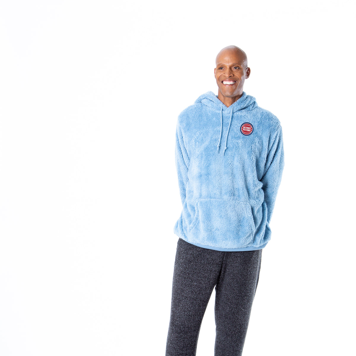 Man facing forward wearing light blue sherpa hoodie with a front kangaroo pocket and drawstring hood, featuring small circular Detroit Pistons embroidery on the left chest.