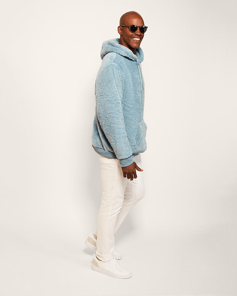 Man wearing a blue hoodie and white pants on a light gray background