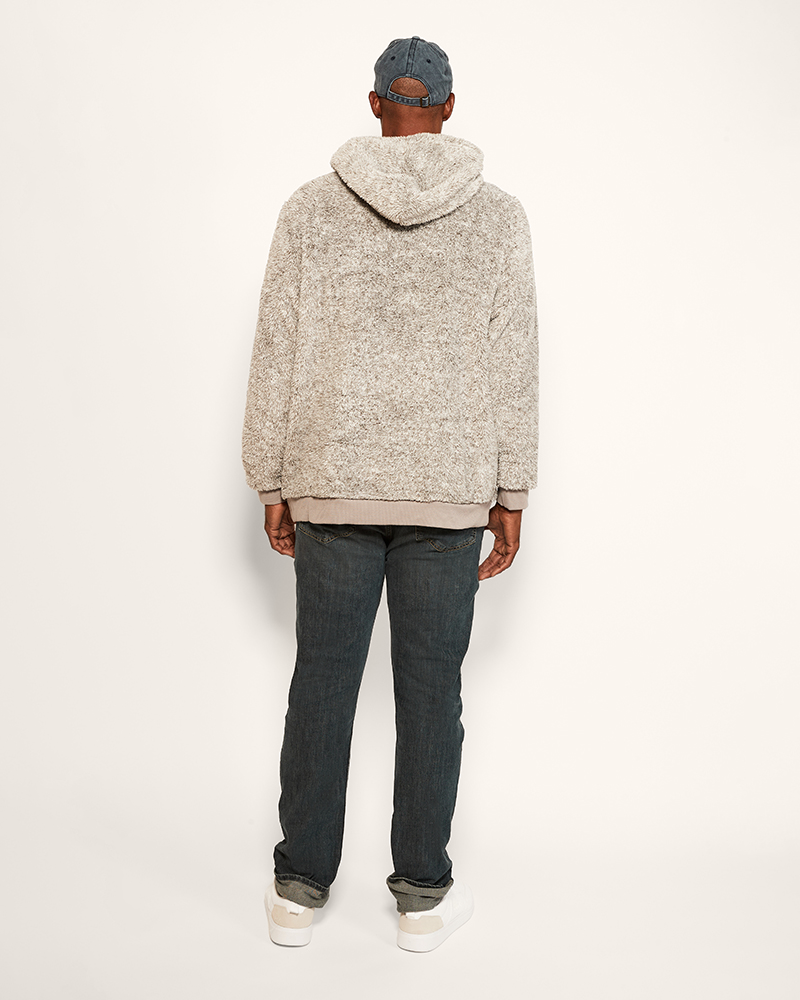 Person wearing a grey hoodie and dark jeans on a white background