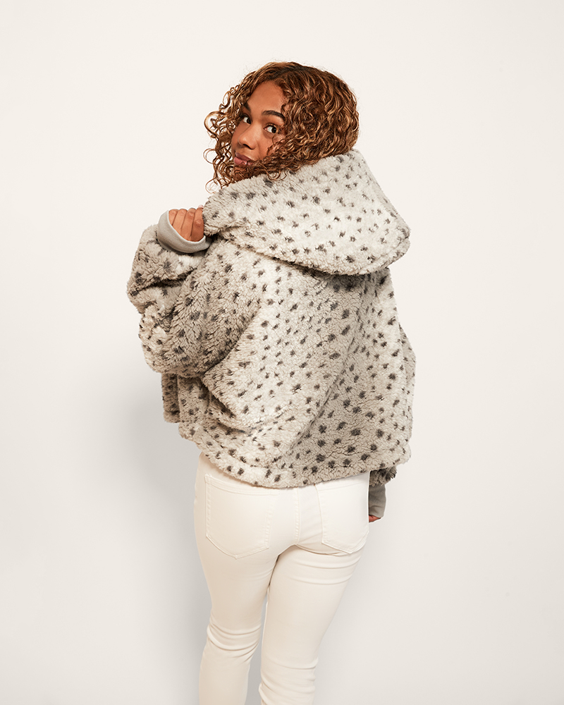Person wearing a patterned jacket and white pants on a plain background
