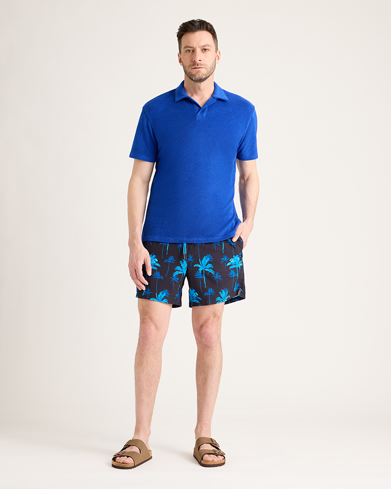 Man wearing a blue polo shirt and patterned shorts on a white background|Model: 5'11" wearing size L