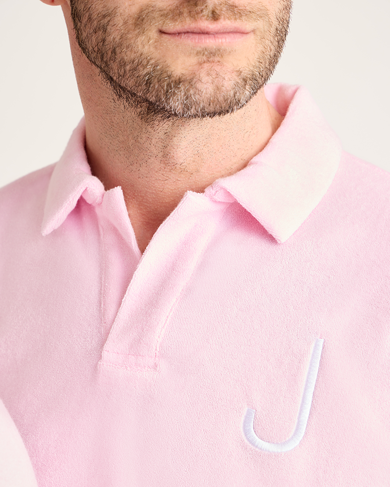 Close-up of a person wearing a light pink polo shirt with a brand logo on a white background|Model: 5'11" wearing size L