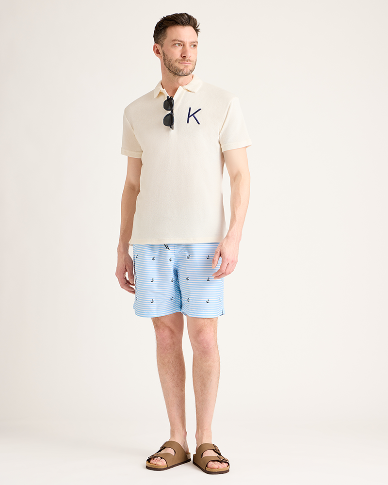 Man wearing a cream polo shirt with a logo and blue striped shorts on a white background|Model: 5'11" wearing size L