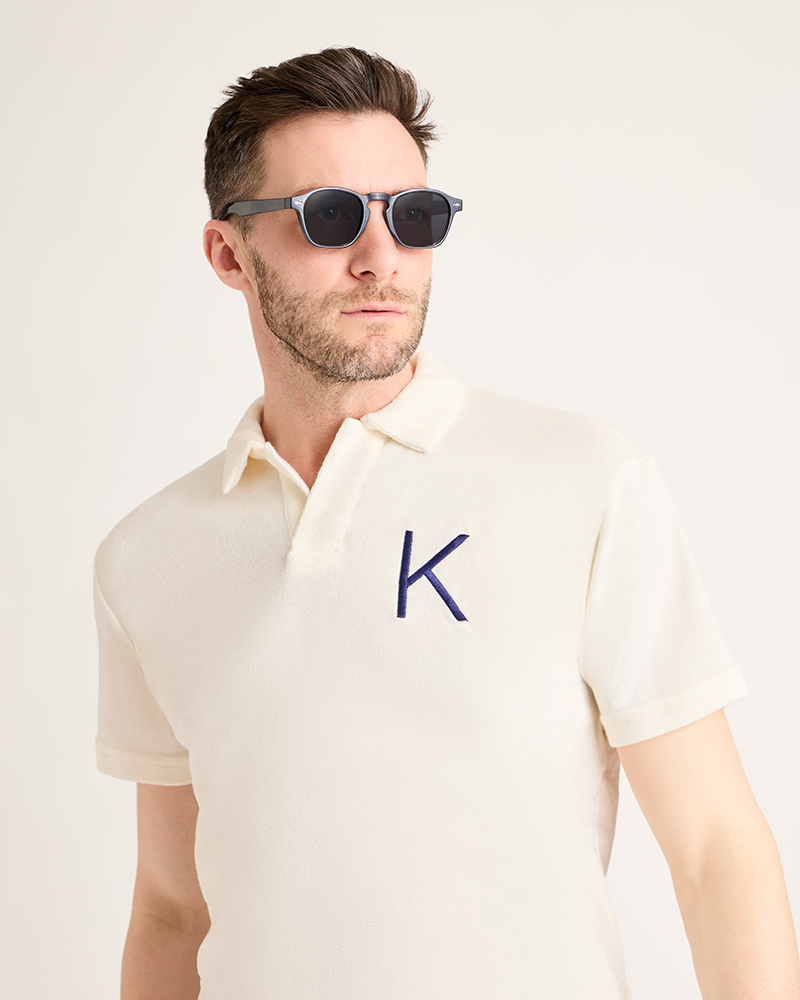 Man wearing a cream polo shirt with a blue 'K' logo on a white background|Model: 5'11" wearing size L