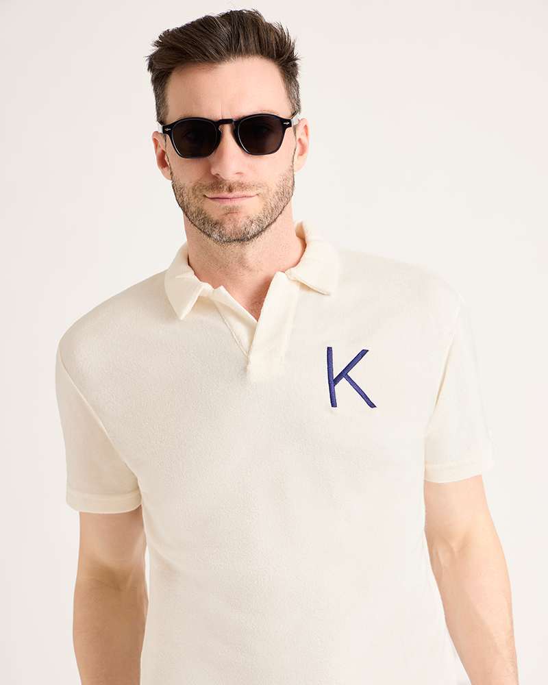 Man wearing a cream polo shirt with a blue 'K' logo on a light background|Model: 5'11" wearing size L