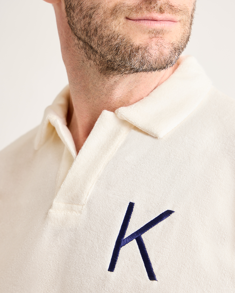 Close-up of a cream-colored polo shirt with a blue embroidered letter 'K' on a plain background|Model: 5'11" wearing size L