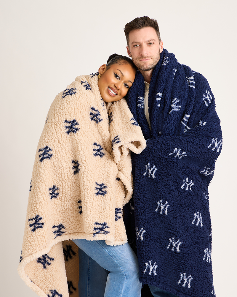 Two people wrapped in New York Yankees-themed blankets against a plain background