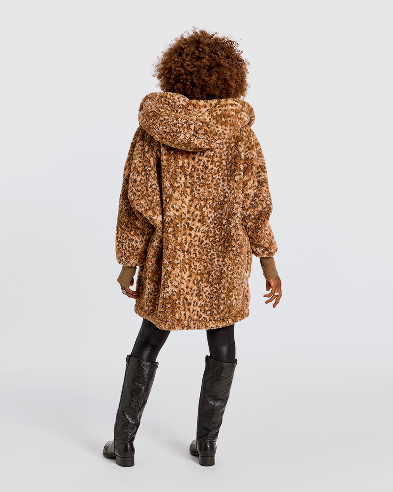 A model viewed from behind wearing a brown and tan leopard-print faux fur coat with a hood, paired with black leggings and black knee-high boots, against a light gray studio background.|Model is 5'7" wearing size XS/S