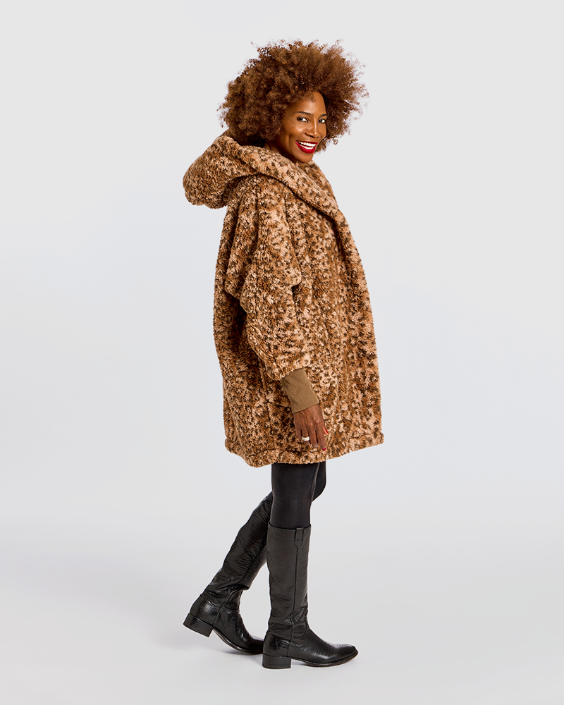 A woman modeling a brown and black leopard-print hooded coat, paired with black boots and leggings, against a plain light gray studio background.|Model is 5'7" wearing size XS/S