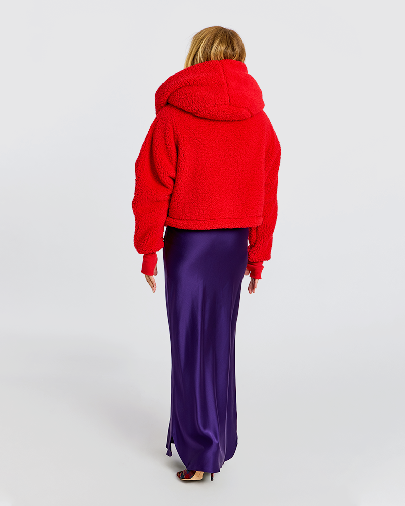 A model viewed from behind wearing a bright red sherpa cropped hoodie and a long, shiny purple satin maxi skirt against a light gray studio background.|Jill is 5'6" wearing size XS/S