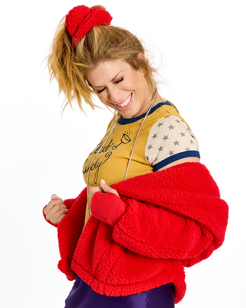 A woman modeling a bright red sherpa fleece jacket with matching red knit cuffs and a red fuzzy hair tie, worn over a yellow graphic top and purple pants against a white background.|Jill: 5'6" in size XS/S