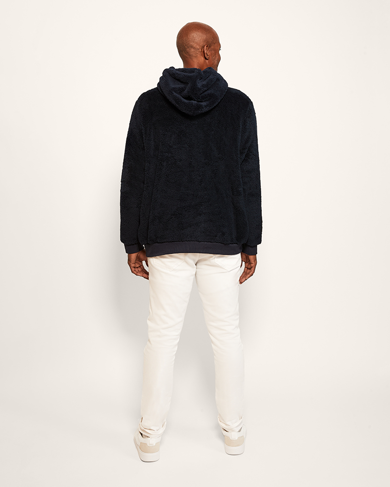 Person wearing a navy hoodie and white pants on a light gray background